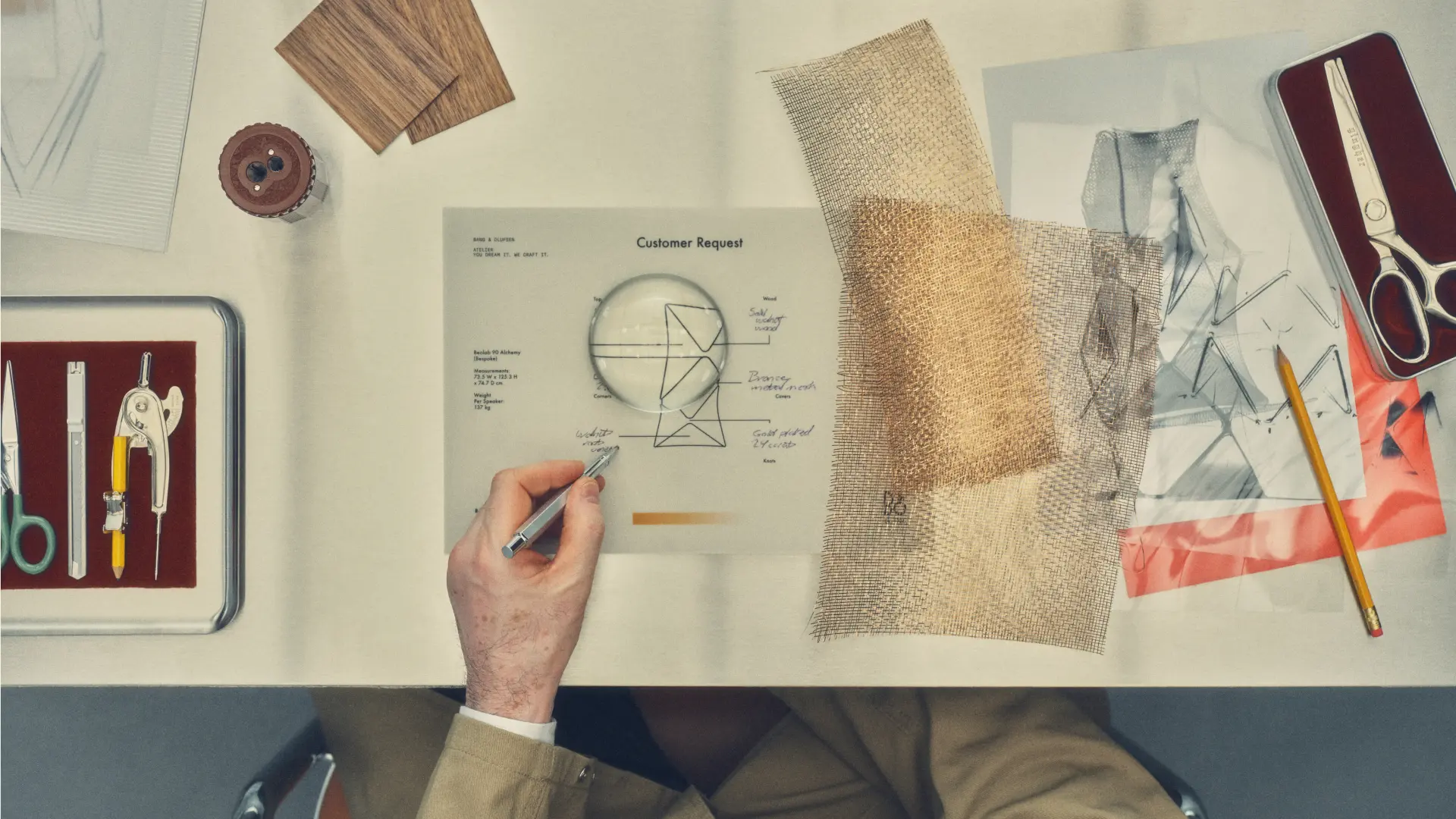 Bang & Olufsen Atelier order worksheet on a drafting desk — a one-of-one Beolab 90 sketch surrounded by walnut veneer, bronze mesh and gold-plated web samples