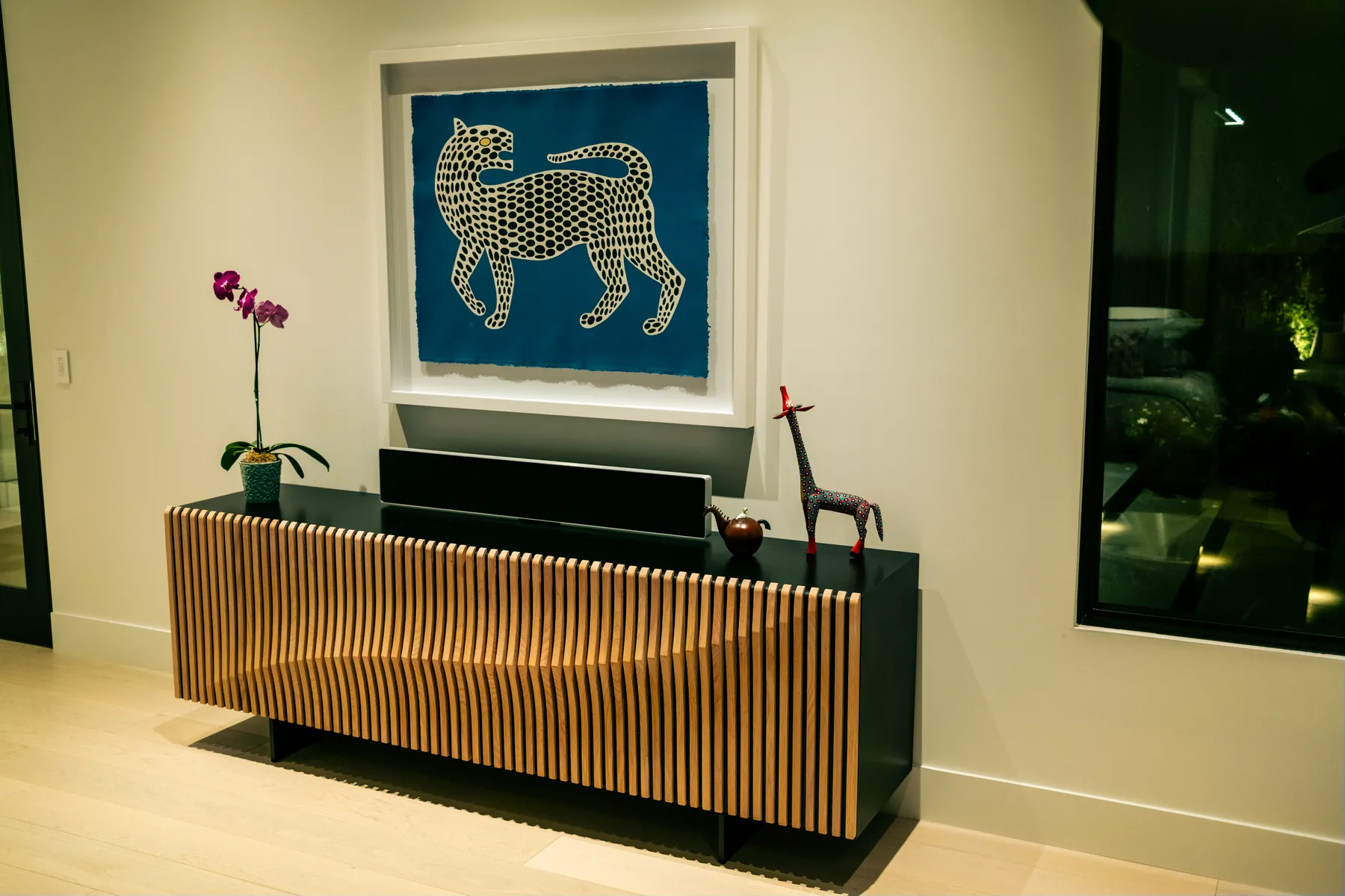 Bang & Olufsen Beosound Stage soundbar on a slatted-wood credenza beneath framed art in a Watt Integration project home — the technology receding into the architecture