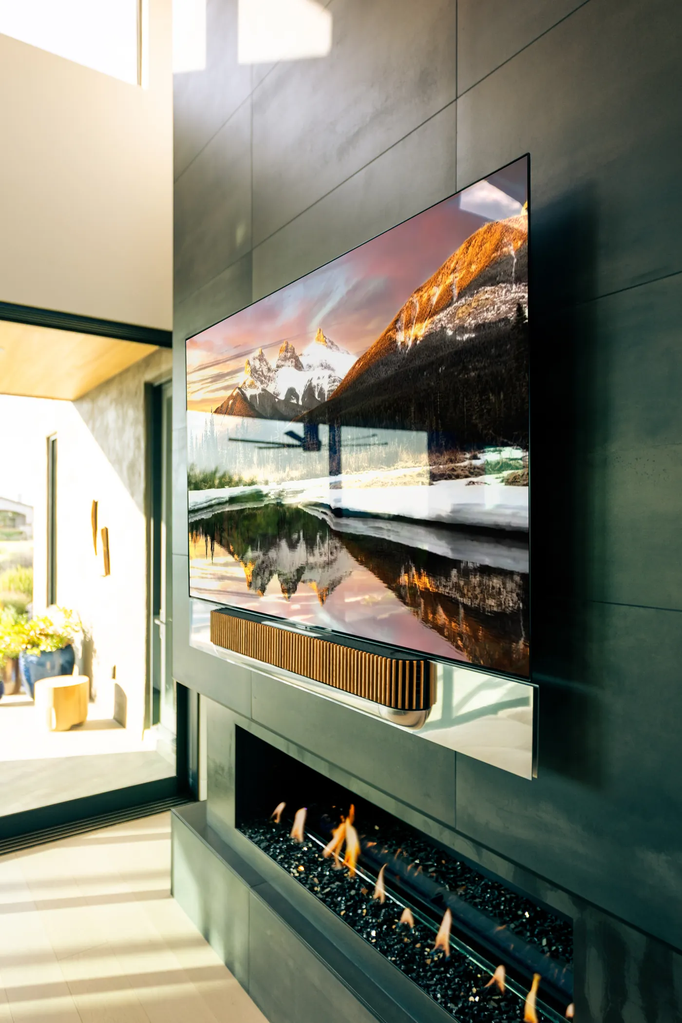 Bang & Olufsen Beosound Theatre soundbar beneath a wall-mounted TV over a linear fireplace, golden-hour light