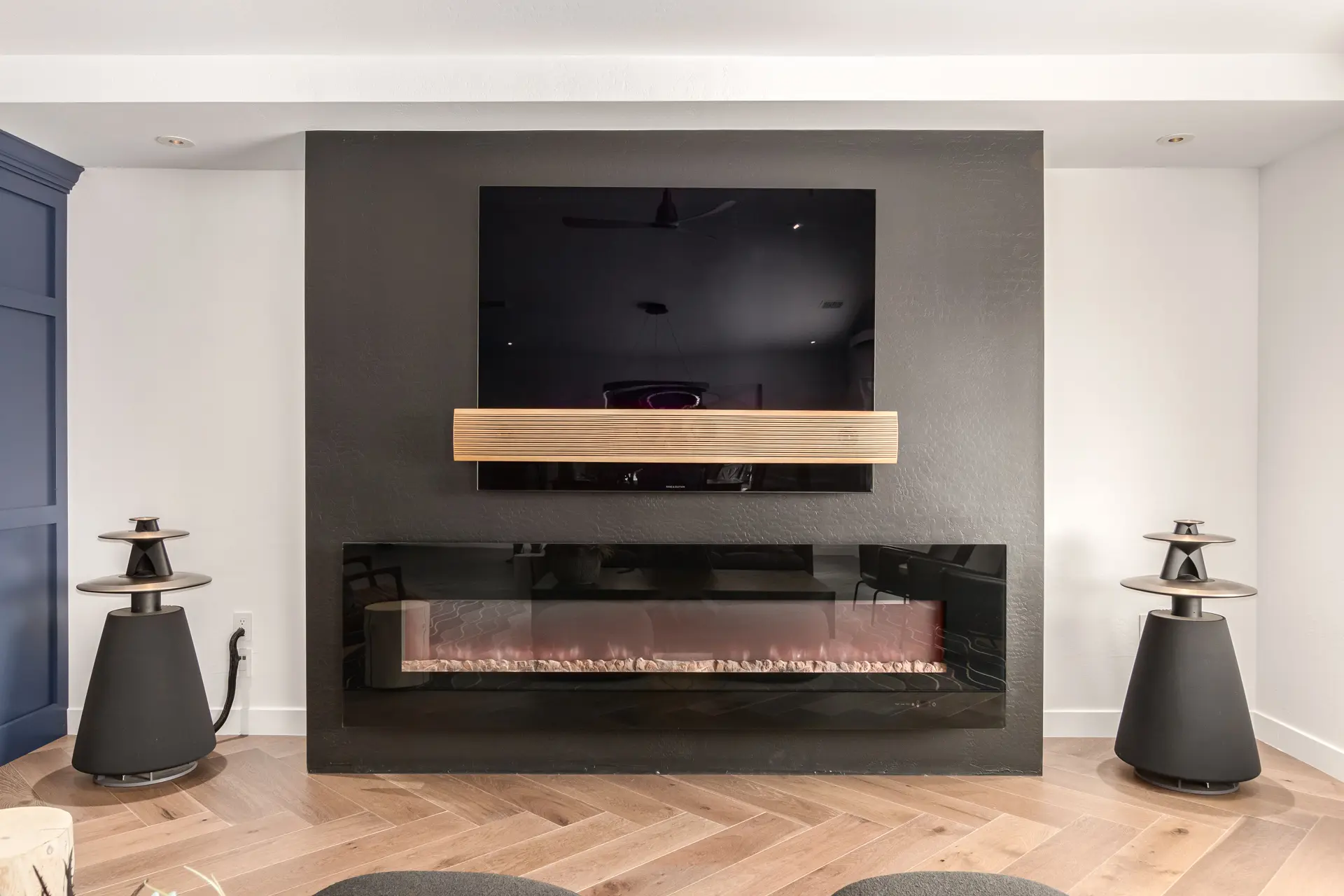 Bang & Olufsen Beovision Eclipse television and Beosound Theatre soundbar on a dark feature wall over a linear fireplace, flanked by a pair of Beolab 5 speakers — Watt Integration home cinema project
