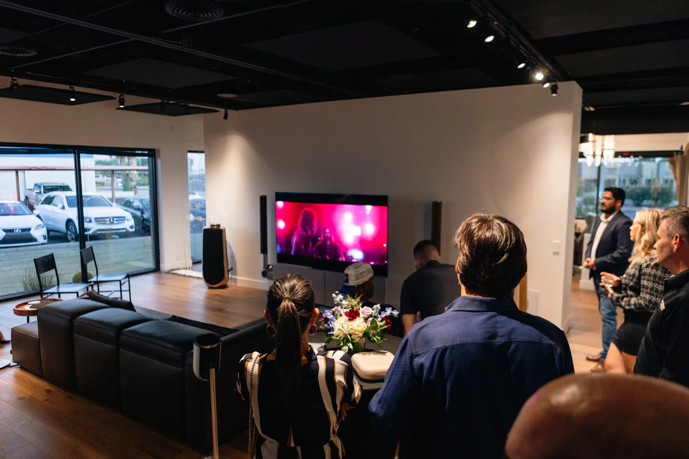 The demo lounge at the Scottsdale showroom during an evening event — a wall-mounted television and floor-standing speakers playing to a seated group