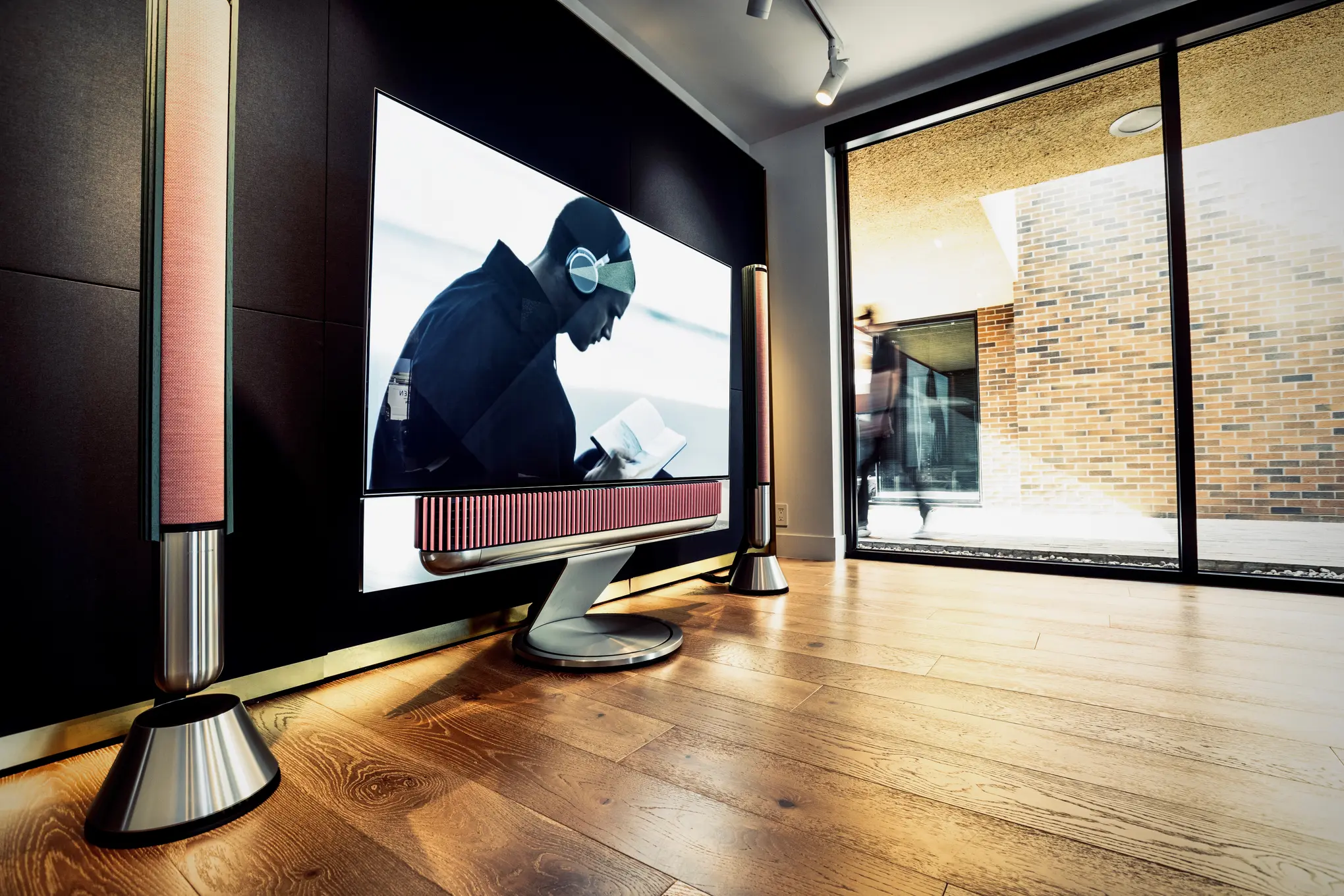 Bang & Olufsen Beovision Harmony flanked by tower speakers on the demo wall of the Scottsdale showroom, the courtyard beyond the glass