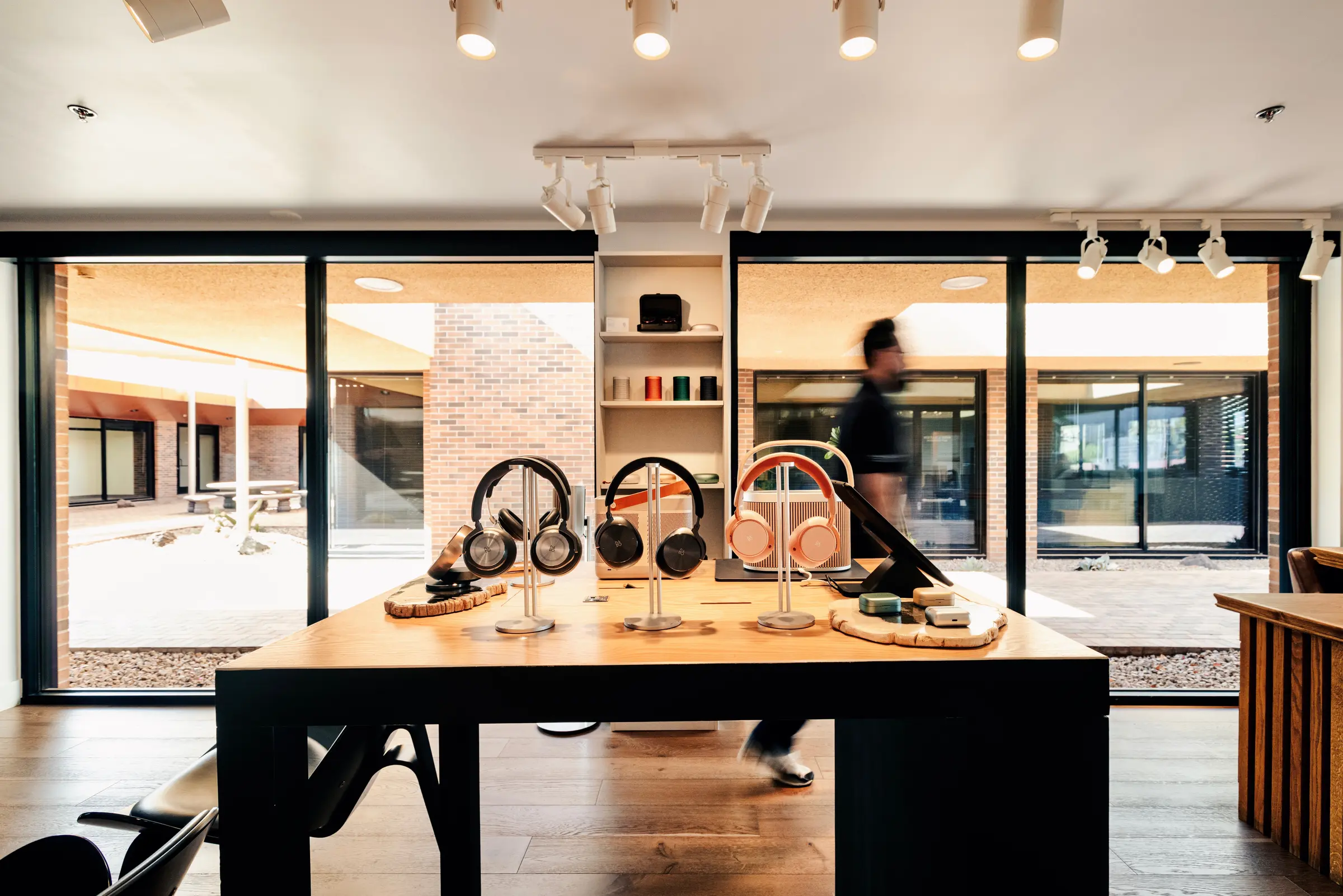 The headphone testing table at the Bang & Olufsen Scottsdale showroom — headphones and earbuds on stands, the courtyard beyond the glass