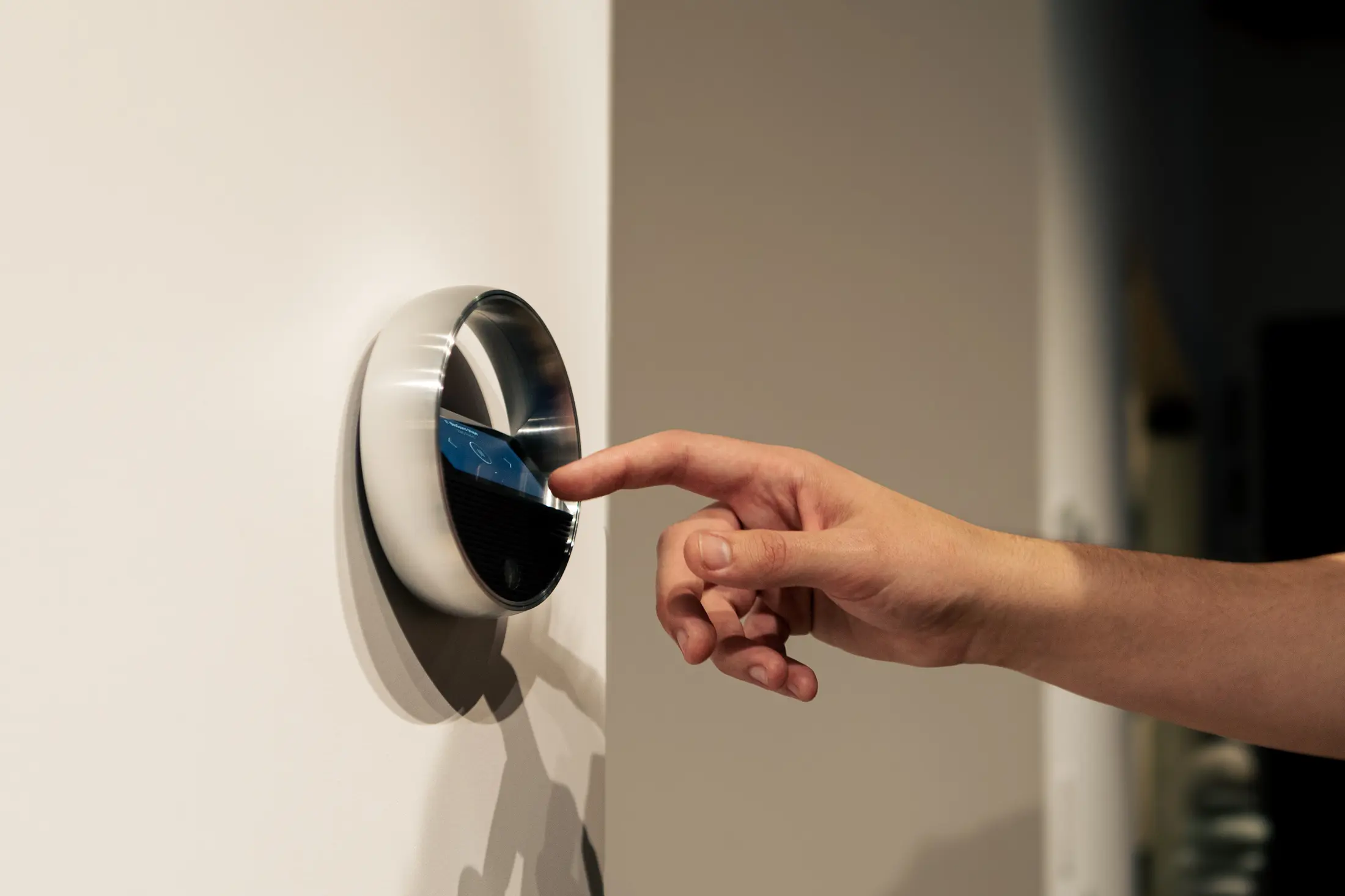 A hand reaching to a round Bang & Olufsen Beoremote Halo control mounted flush on a plain wall