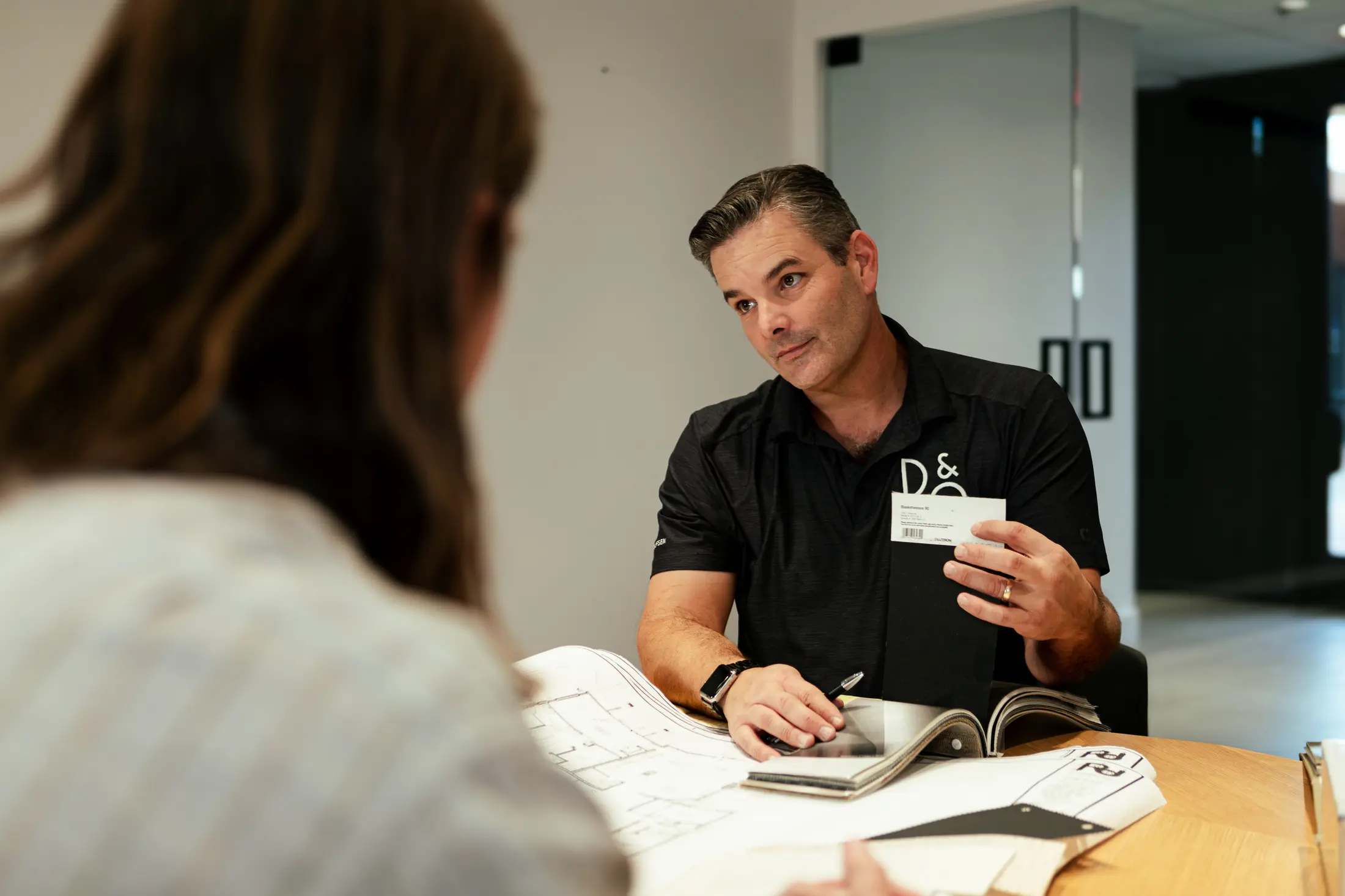 Bryan Watt at the design table with a client, sample card in hand — Watt Integration showroom