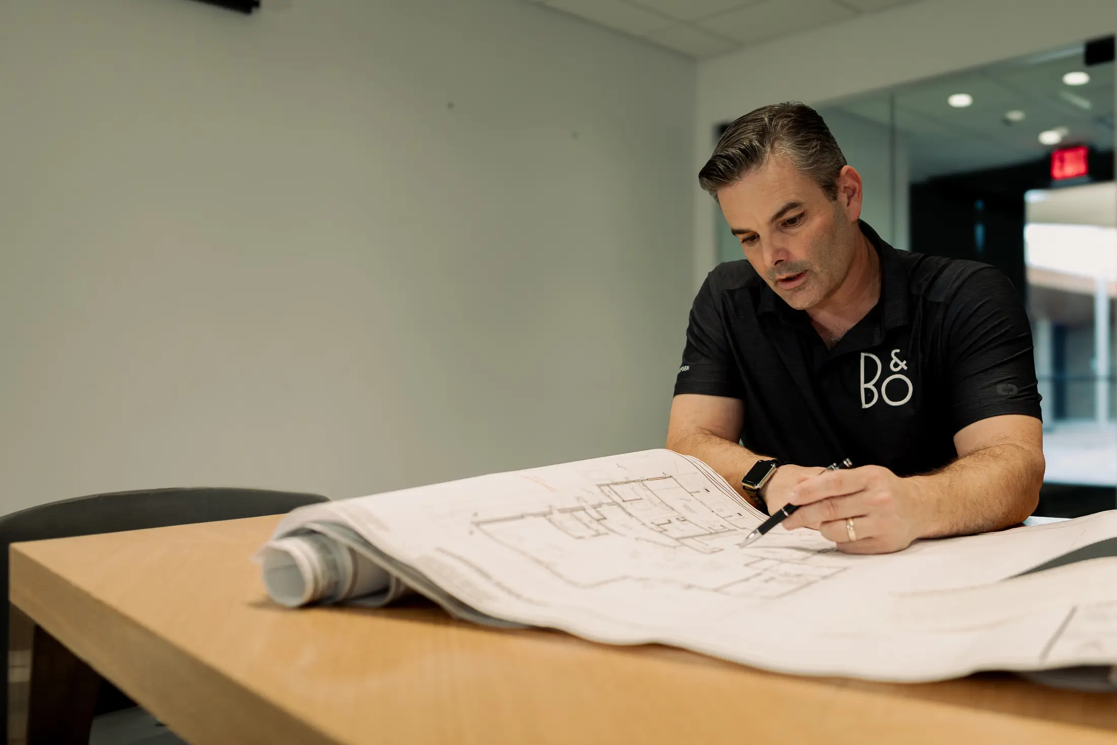 Bryan Watt seated at a table with a rolled plan set open in front of him, pen in hand