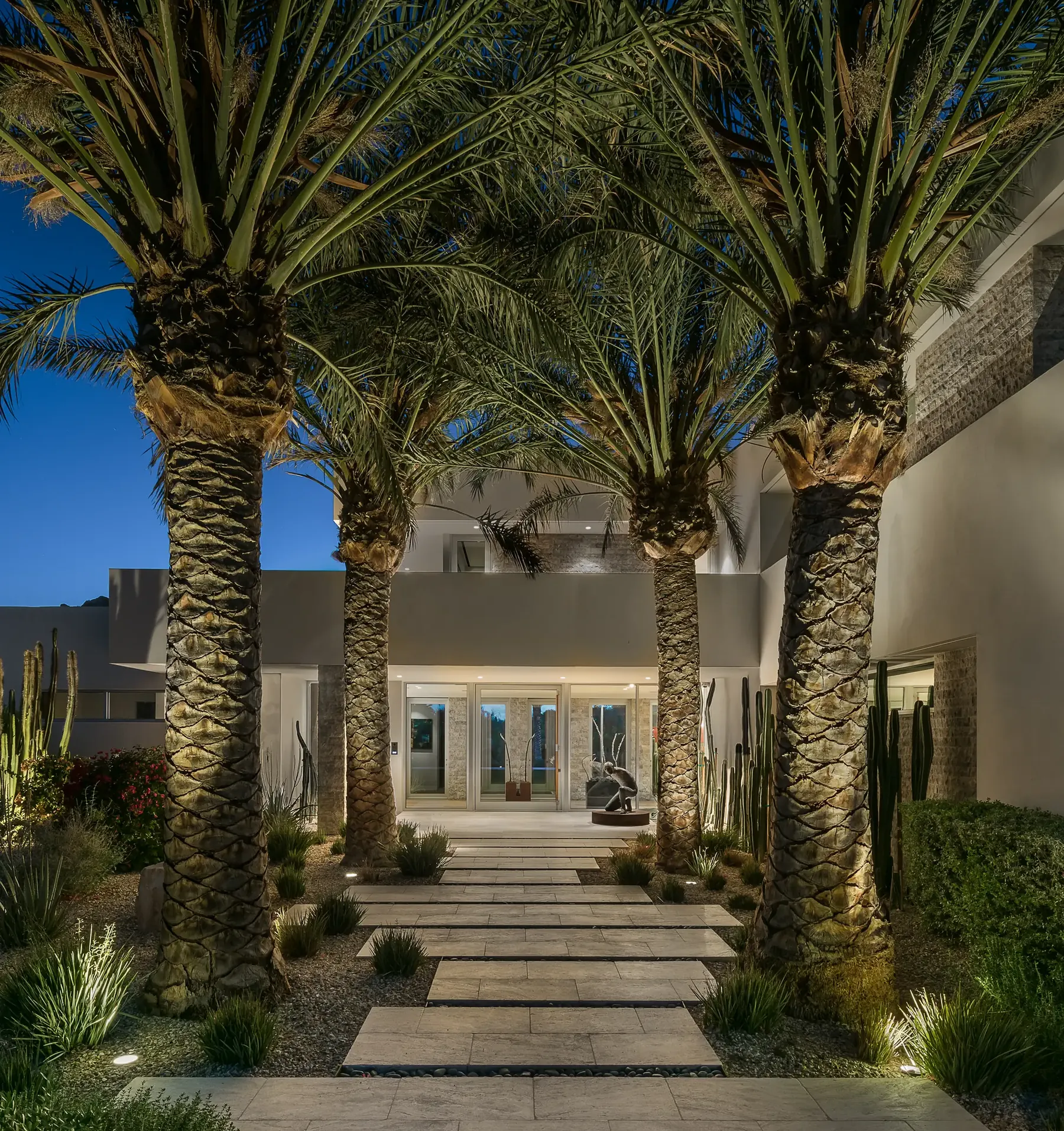 Landscape lighting at dusk — uplit palms and path lights along the front walkway