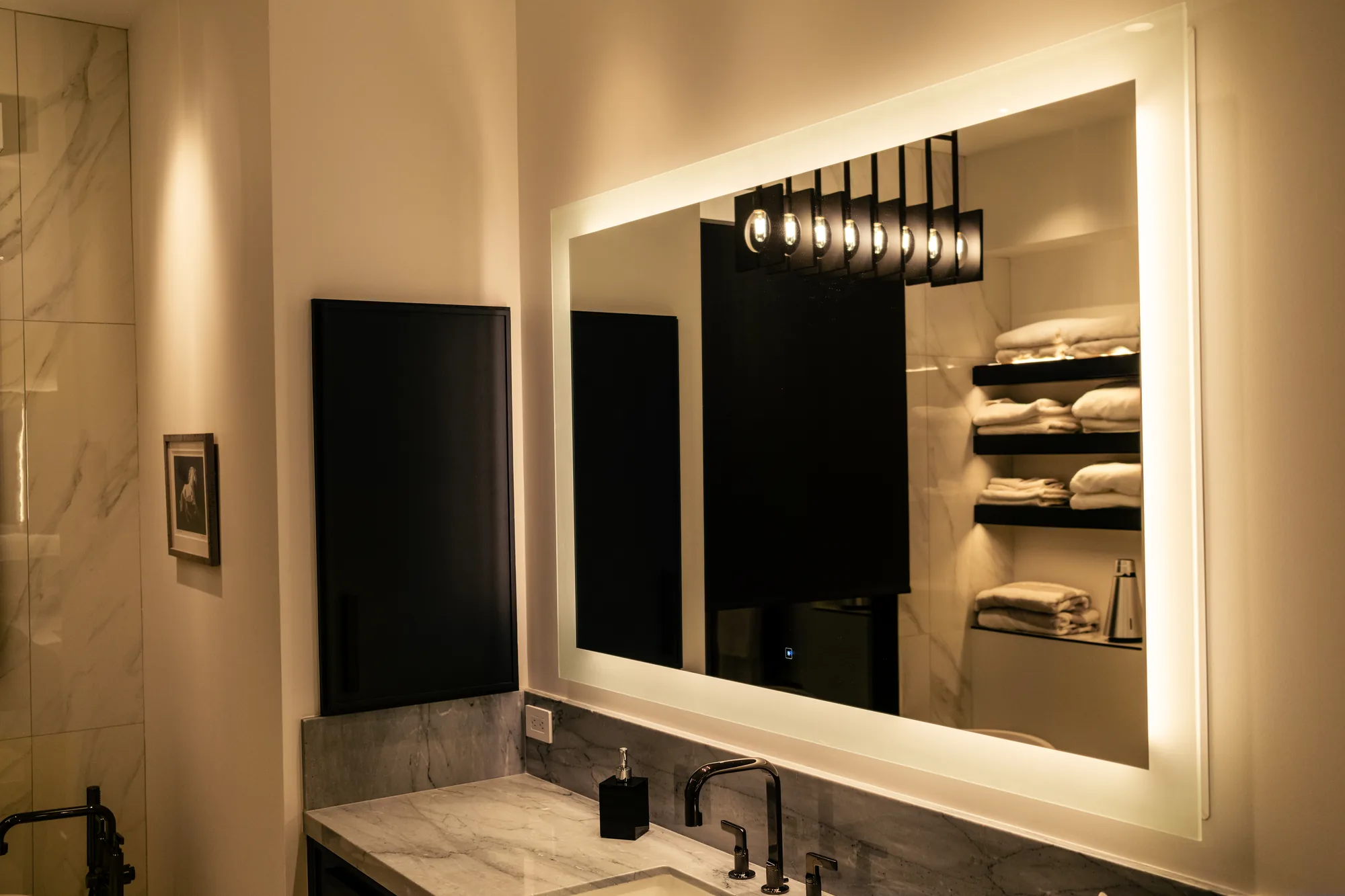 Bathroom vanity with a backlit LED mirror, layered Lutron lighting and an accent-lit towel niche