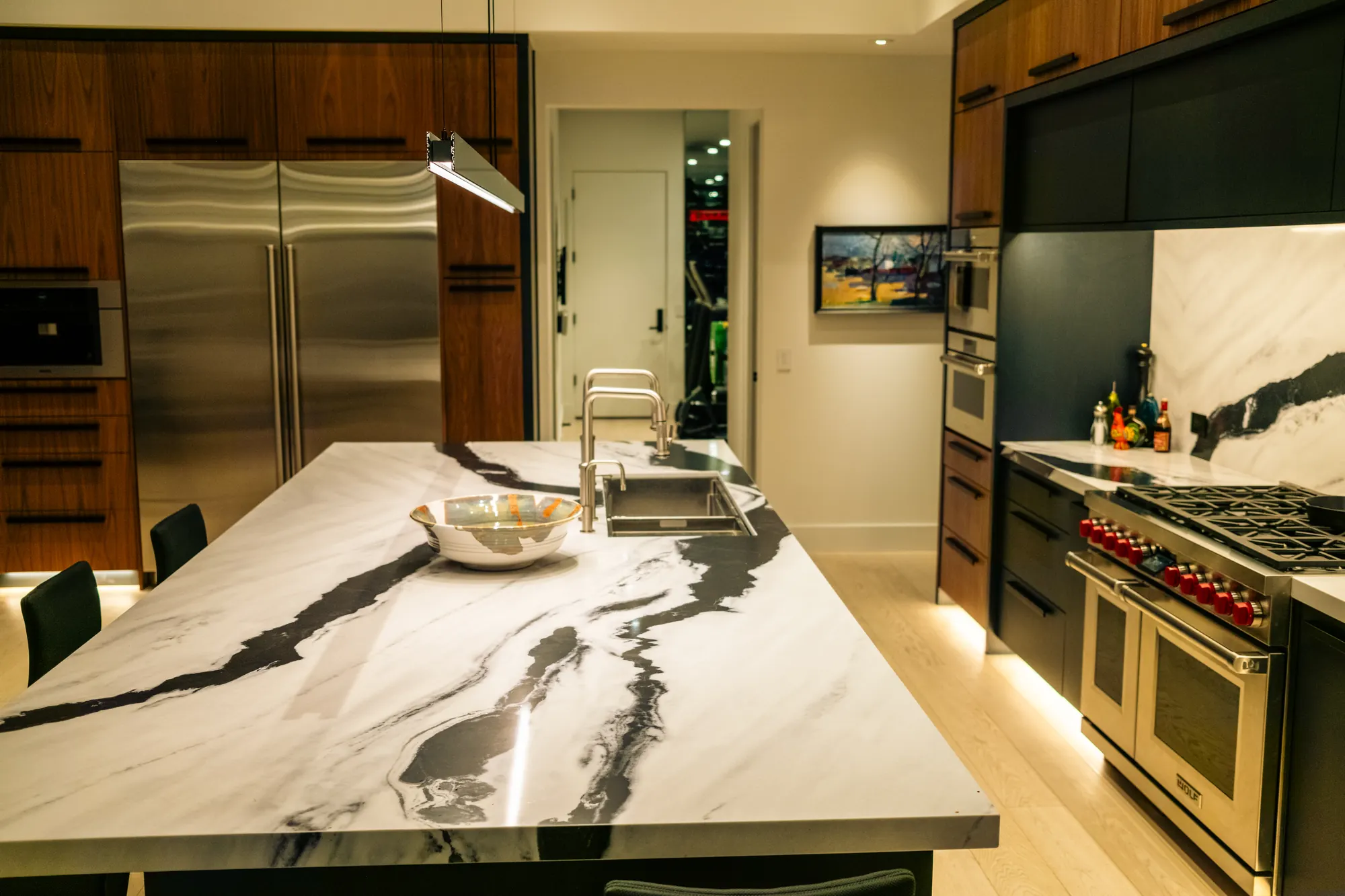 Kitchen with layered LED lighting — under-cabinet, toe-kick and pendant — over a marble island