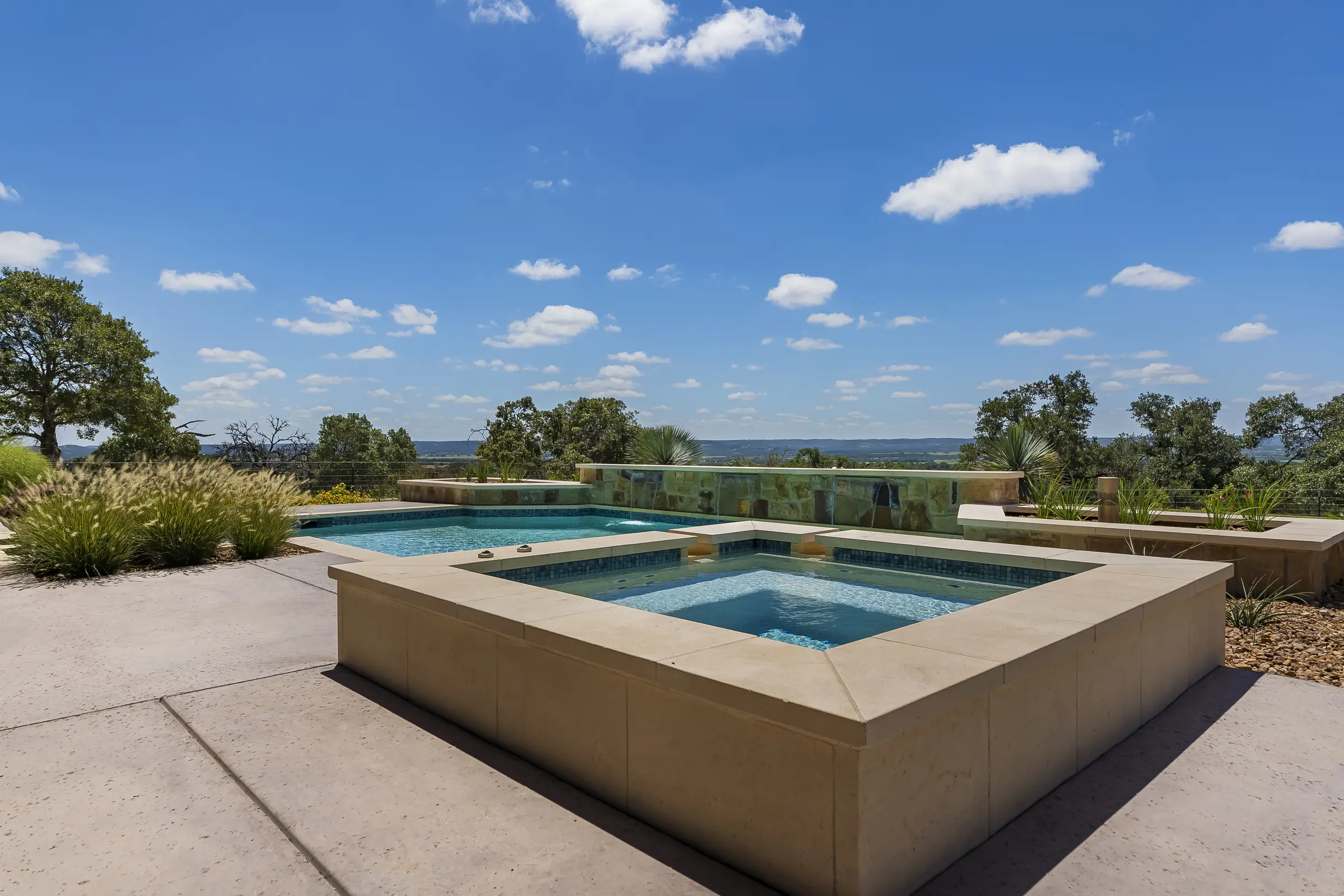 Pool and raised spa on a stone terrace looking out over oaks and open hill country, a bollard speaker set into the coping