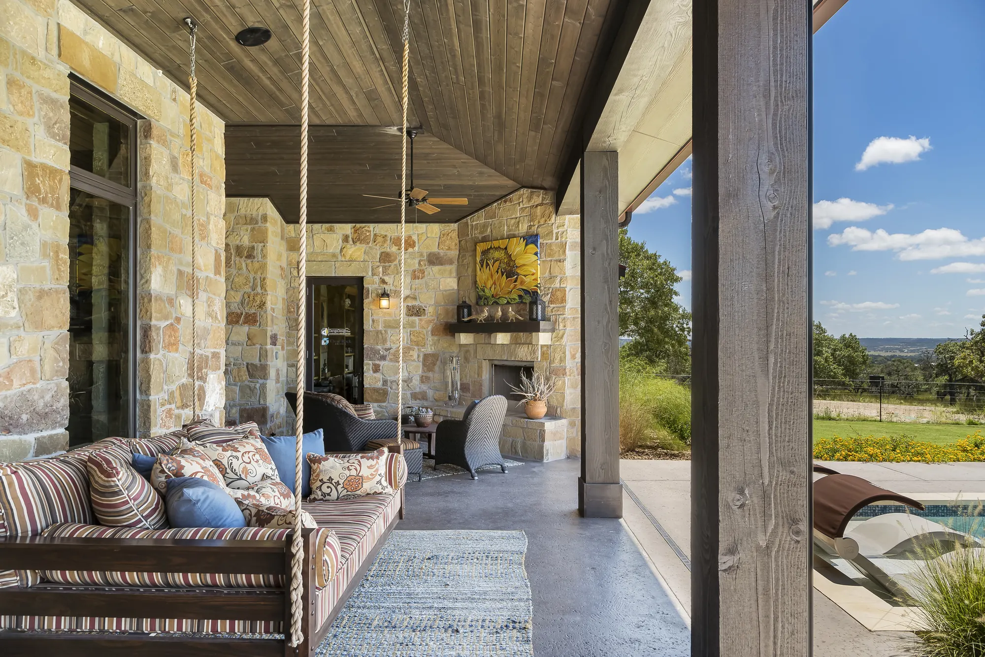 Covered stone patio with a hanging daybed and an in-ceiling outdoor speaker in the wood ceiling