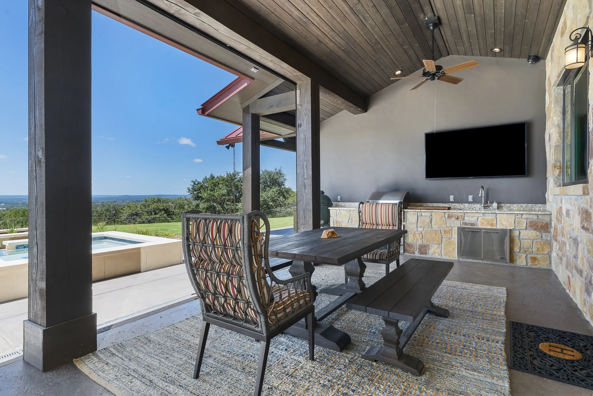 Outdoor dining porch with a wall-mounted weatherproof TV over the outdoor kitchen