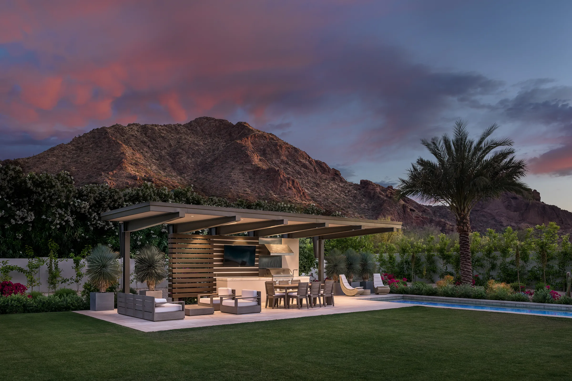 Poolside ramada at dusk with a weatherproof outdoor TV over the outdoor kitchen, mountain backdrop