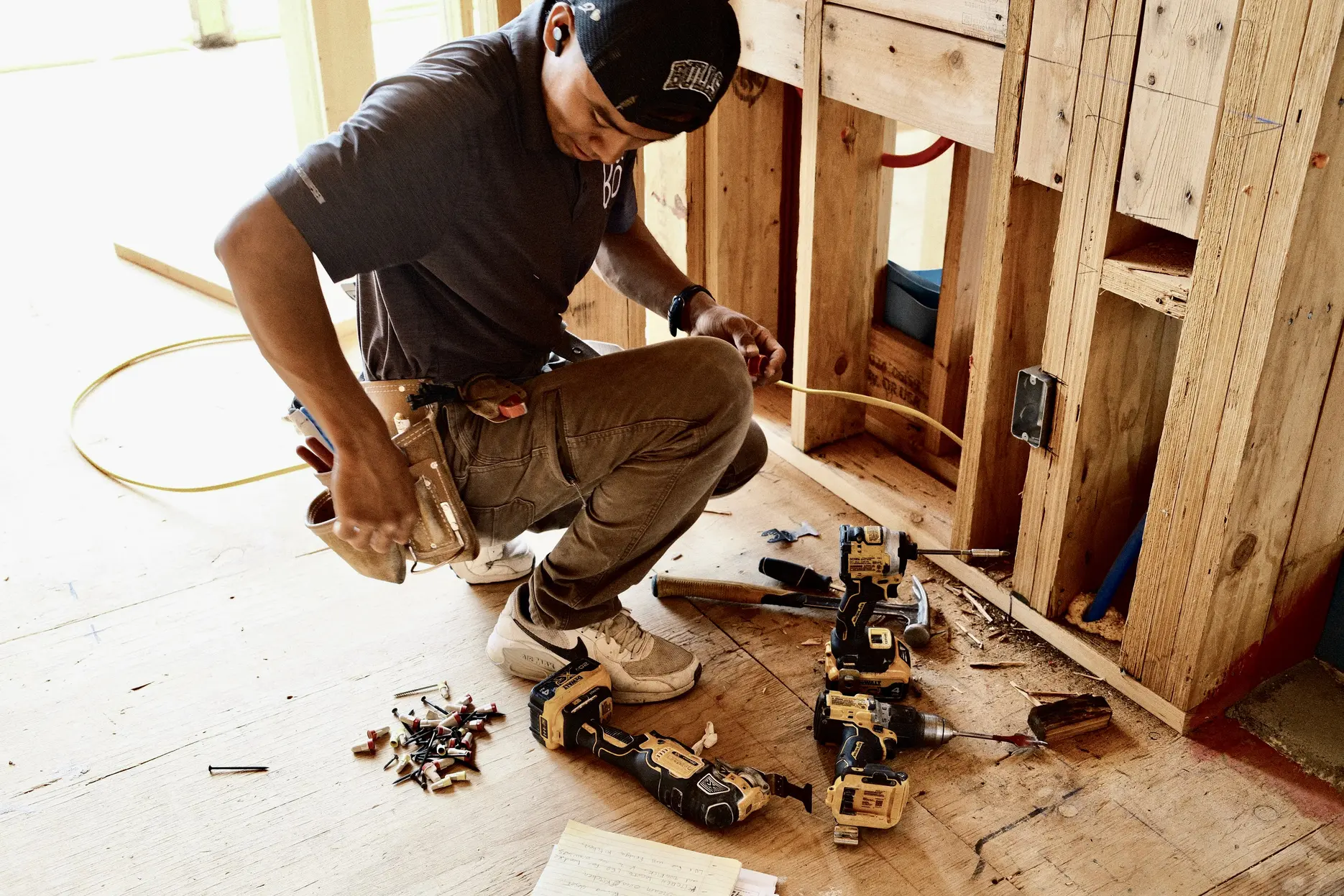 Watt Integration technician pulling low-voltage wire through open framing at a rough-in, tools laid out on the subfloor