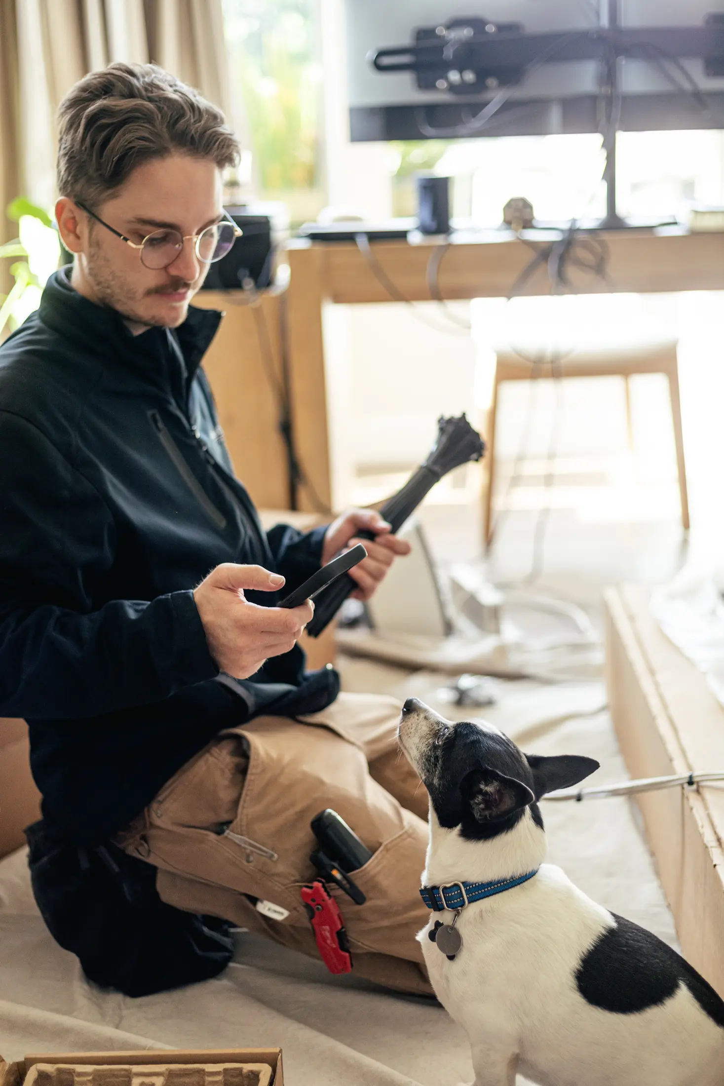 Watt Integration technician kneeling with cable ties during a television installation in a project home, the household's dog looking on