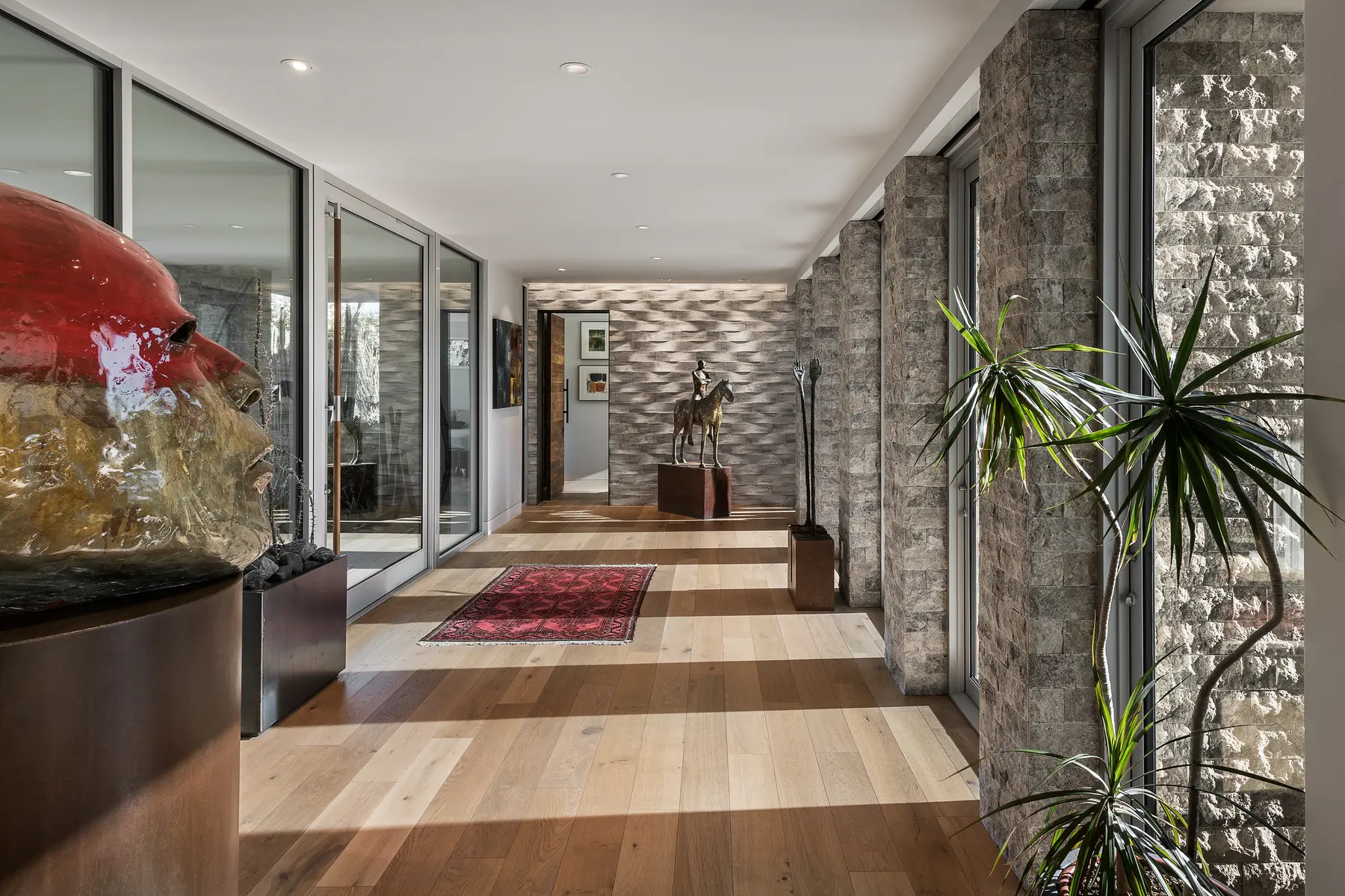 Gallery-style entry hall of a project home with split-stone columns, wide-plank oak floors and collected sculpture